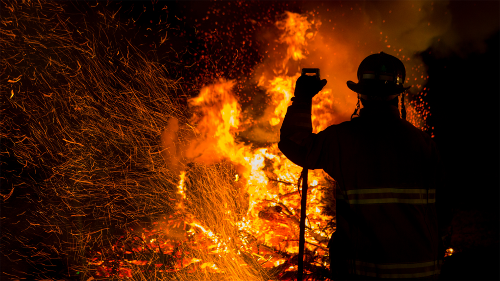 A firefighter in front of a fire gutting property